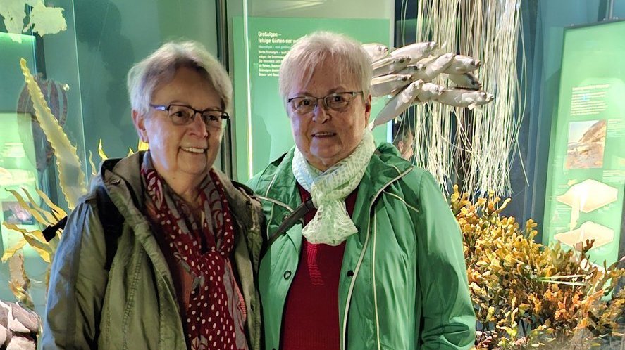 AWG‑Mitglieder stehen vor dem modernen Ozeaneum in Stralsund und lächeln in die Kamera